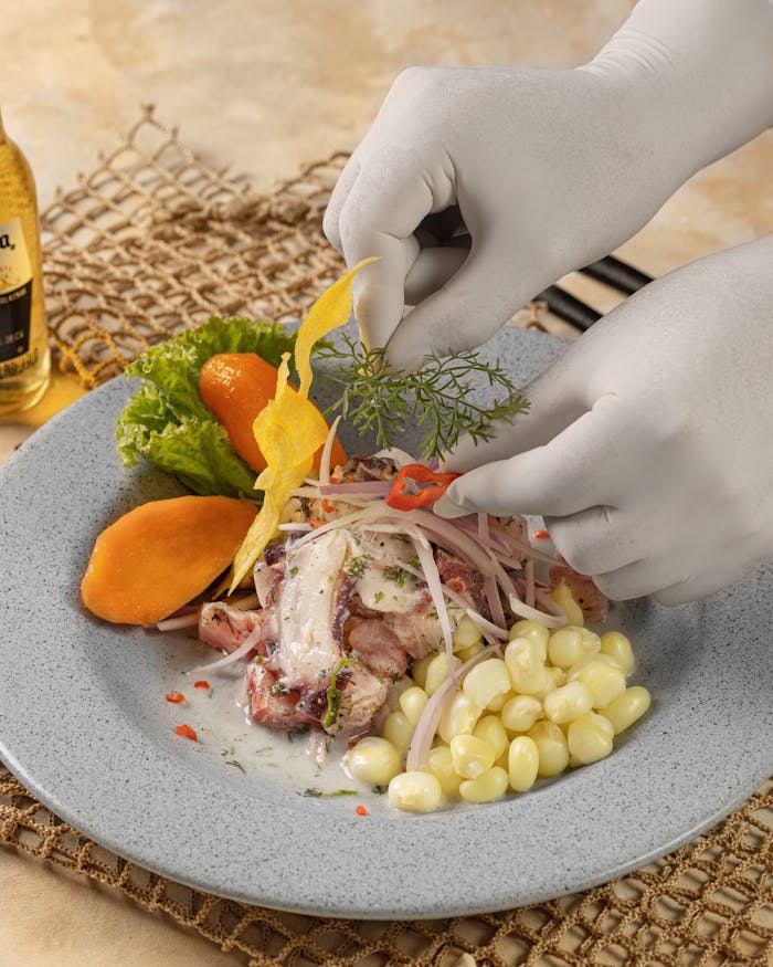 A chef intricately garnishing a classic Peruvian ceviche dish with corn and vegetables.