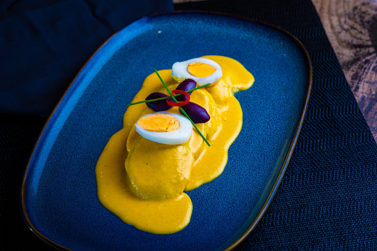 Close-up of Peruvian Papa a la Huancaína on a blue plate with eggs and olives.